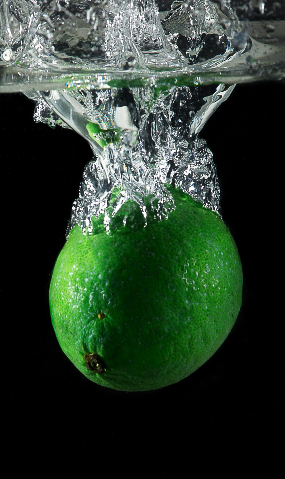 Vibrant green lime creating a splash in water against a black background.